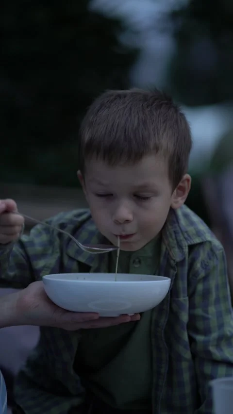 Cute young boy fed soup outdoors at dusk by adult hand Stock-Footage 342968674