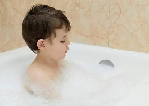 Cute young boy playing with bubbles while taking a bath 写真素材