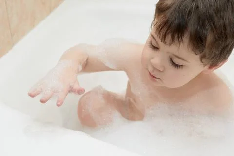 Cute young boy playing with bubbles while taking a bath 写真素材
