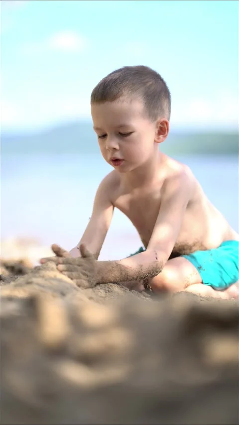 Cute young boy playing with sand on a sunny beach by the lake  Stock Footage 342179369