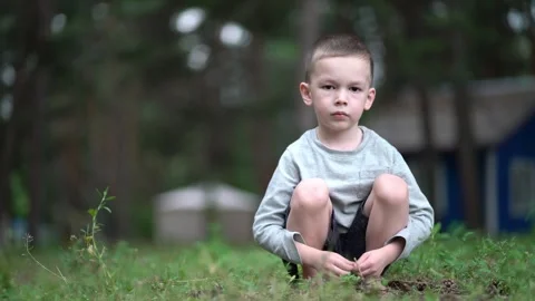 Cute young boy sits barefoot on green grass outdoors Video stock 342179348