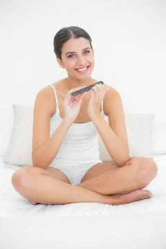 Cute young brown haired model in white pajamas filing her nails Stock Photos