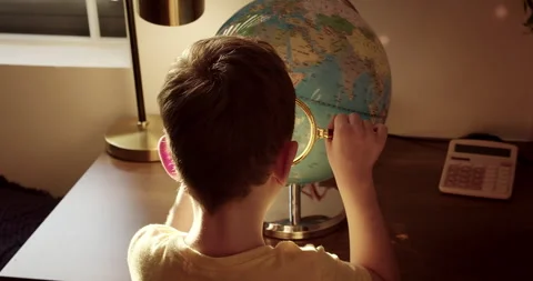 Cute young child looking closely at a globe through a magnifying glass. Back Stock Footage 313079230