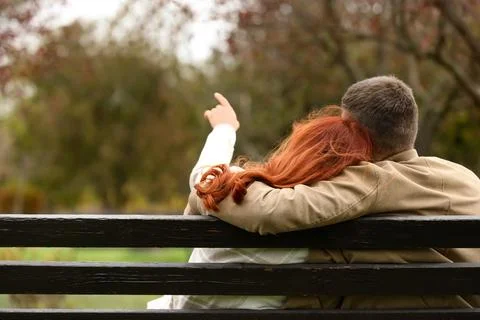 Cute young couple hugging while sitting on bench in autumn park, back view Stockfoto's