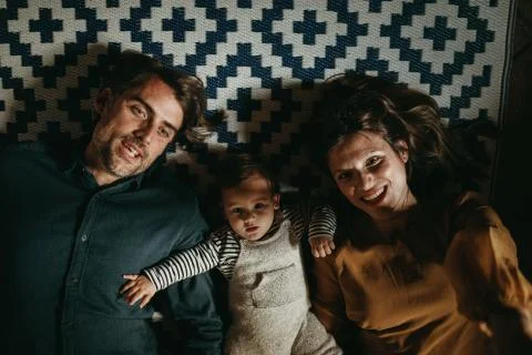 Cute young couple lying down with their baby son in the floor at home Stock Photos