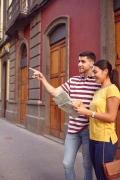 Cute young couple studying a map and pointing to their front while smiling ha Stock Photos