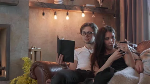 Cute Young Couple A Young Guy Reading A Book A Young Girl Using A Smartphone Stock Footage 138017498