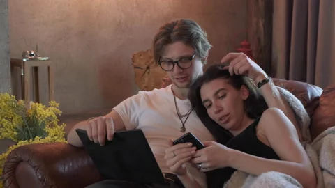 Cute Young Couple A Young Guy Reading A Book A Young Girl Using A Smartphone Stock Footage 138018650