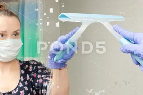 Cute young girl maid in medical mask cleans bathroom mirror during coronaviru Stock Photos