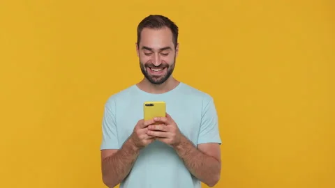 Cute young guy 20s in basic casual blue t-shirt hold in hand using mobile cell Video stock 148290679