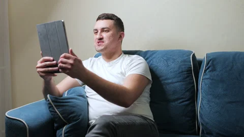A cute young guy communicates on a tablet, a video call. Man waves his hand at Stock Footage