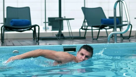 Cute young guy swims in the hotel pool with blue water on vacation Stock Footage 102655713