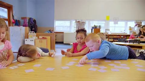 Cute young kids sit around a table at school and play a learning game Stock Footage 34004646