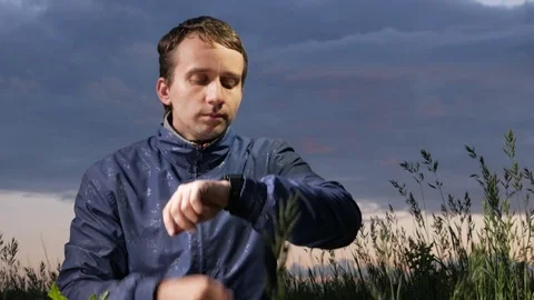 A cute young man checks the messages on a smartwatch at sunset on the field Stock Footage 76971248