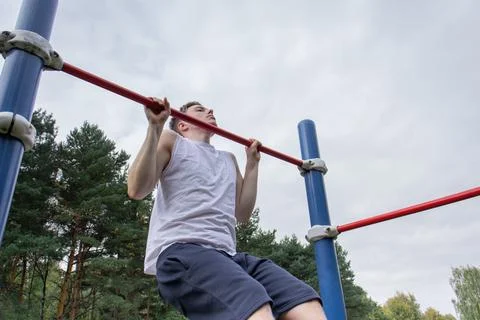 A cute young man is doing exercises on a horizontal bar at the stadium Stock Photos