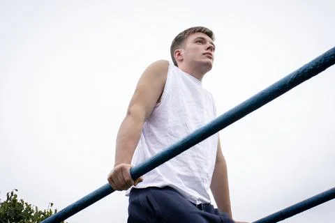 A cute young man doing exercises on the uneven bars at the stadium Stock Photos