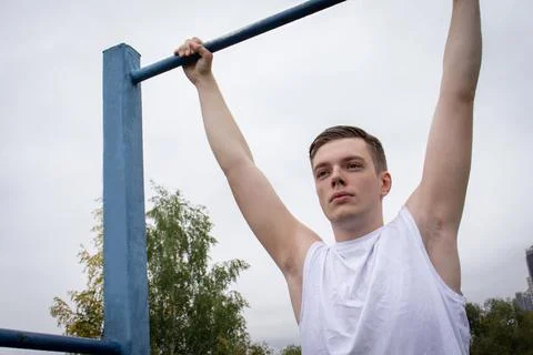 A cute young man is doing exercises on a horizontal bar at the stadium Stock Photos