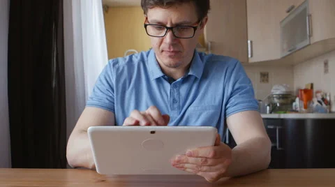 A cute young man uses a tablet PC and thinks at home Видео 60570918