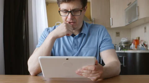 A cute young man uses a tablet PC and thinks at the table at home Vídeos de archivo 66466544