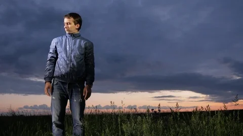 A cute young man waves off mosquitoes at sunset on the field. Beautiful sky on a Stock Footage 76992168