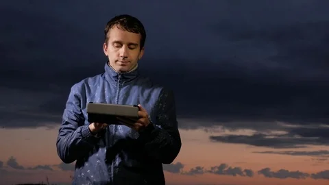 Cute young man working on a tablet computer at sunset on the field. Beautiful Stock Footage 76950213