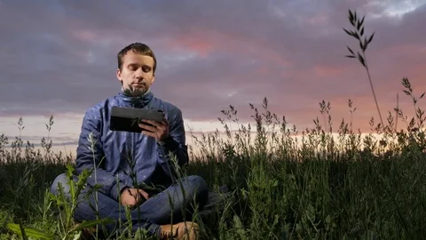 Cute young man working on a tablet computer at sunset on the field. Beautiful Stock Footage 76950616