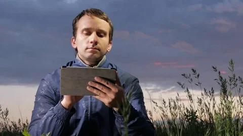 Cute young man working on a tablet computer at sunset on the field. Beautiful Stock Footage 76991764