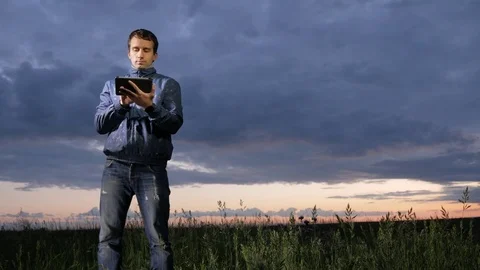 Cute young man working on a tablet computer at sunset on the field. Beautiful Stock Footage 76992017