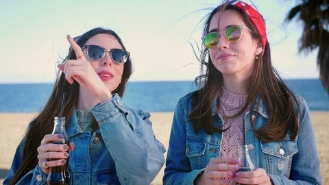 Cute young sisters stand and drink tasty Eco lemonade on the beach side, wearing Stock Footage 106194971