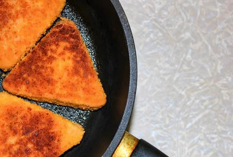 Cutlets of triangular shape are fried in a frying pan. Stock Photos