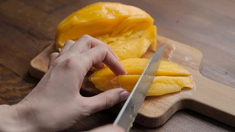 Cuts a ripe yellow mango into pieces  Stock Footage 129129289