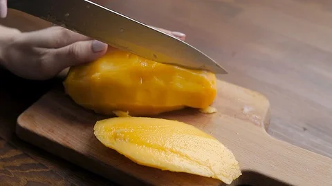 Cuts a ripe yellow mango into pieces  Stock Footage 129129293