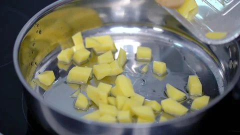 Cutted dice raw potatoes is poured out of a container with shovel into metal pan Stockbeeldmateriaal 260740344