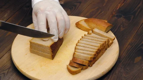 Cutting black bread into slices. Hands in white gloves cut a loaf Stock Footage 219750480