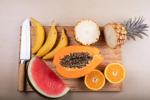 A cutting board with cut fruit on top and a knife, a papaya, a watermelon, .. Stock Photos