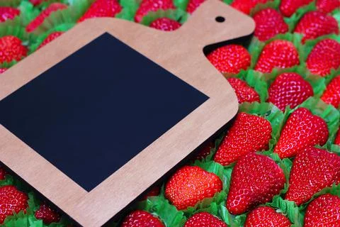 A cutting board with a place for text is placed on a strawberry background. Stock Photos
