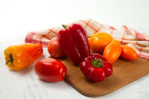 Cutting board with several red and yellow tomatoes and bell pepper on white.. Stock Photos