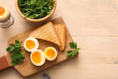 Cutting board with soft boiled eggs, parsley and slices of bread on white woo Stock Photos