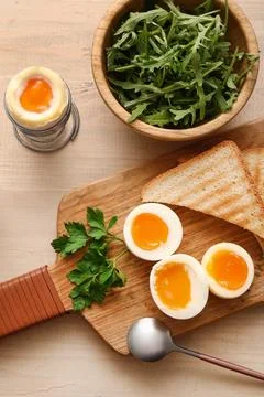 Cutting board with soft boiled eggs, parsley and slices of bread on white woo Stock Photos