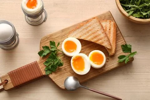 Cutting board with soft boiled eggs, parsley and slices of bread on white woo Stock Photos