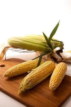 Cutting board with three cobs sweet corn on white wooden background.. Stock Photos