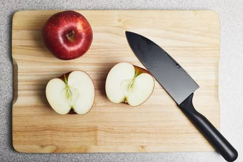 Cutting board with two red apples and a knife on it. One apple is whole, anot Stock Photos