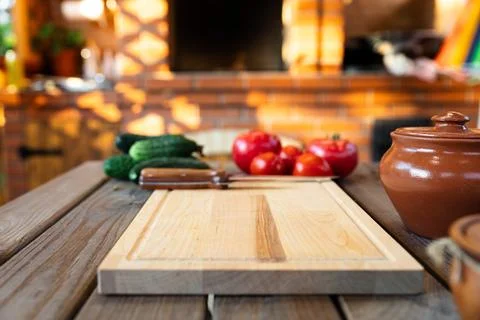 Cutting board on a wooden table, surrounded by fresh vegetables like tomatoes Stock Photos