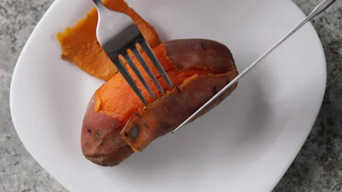 Cutting boiled and hot sweet potato with knife and fork on white plate Stock Footage 151344027