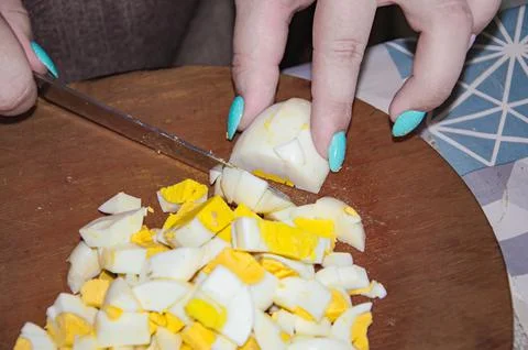 Cutting boiled eggs into slices. Harvesting products for a salad, on a wooden Stock Photos