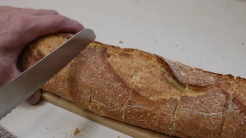 Cutting bread in a kitchen with a sharp knife on a wooden board 库存影片 323606061