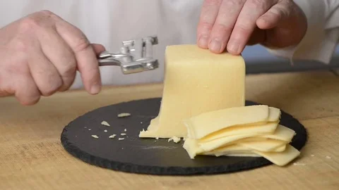 Cutting of cheese into thin slices by means of a cheese slicer on a round Stock Footage 77970131