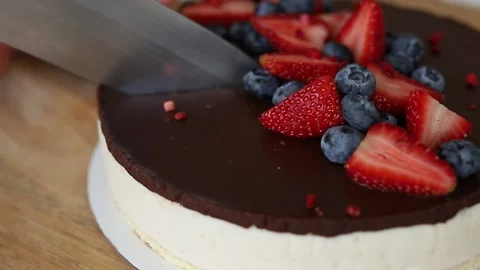 Cutting cheesecake with chocolate icing and strawberries and blueberries Stock Footage 142492475