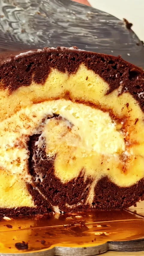 Cutting chocolate roll cake with creamy vanilla swirl filling on a golden Stock Footage 337183361