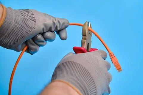 Cutting a computer network wire with wire cutters, blue studio background Stock Photos
